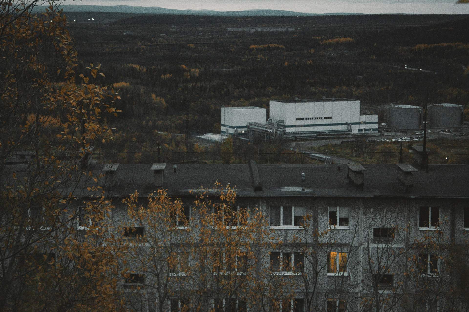 Промышленная площадка с резервуарами и жилой дом на окраине города осенью